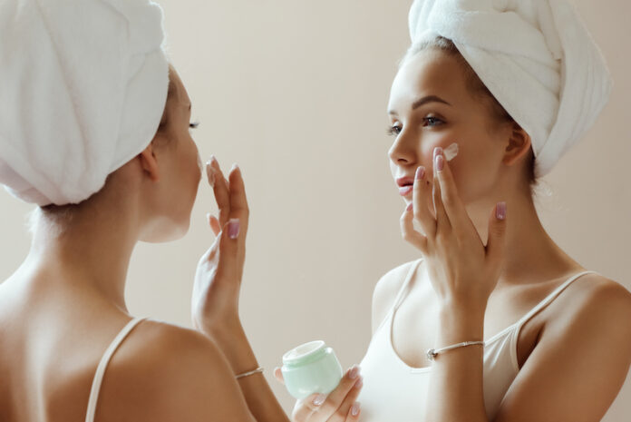 Young attractive woman applying cream to her face while looking at her reflection in the mirror. Beauty photography
